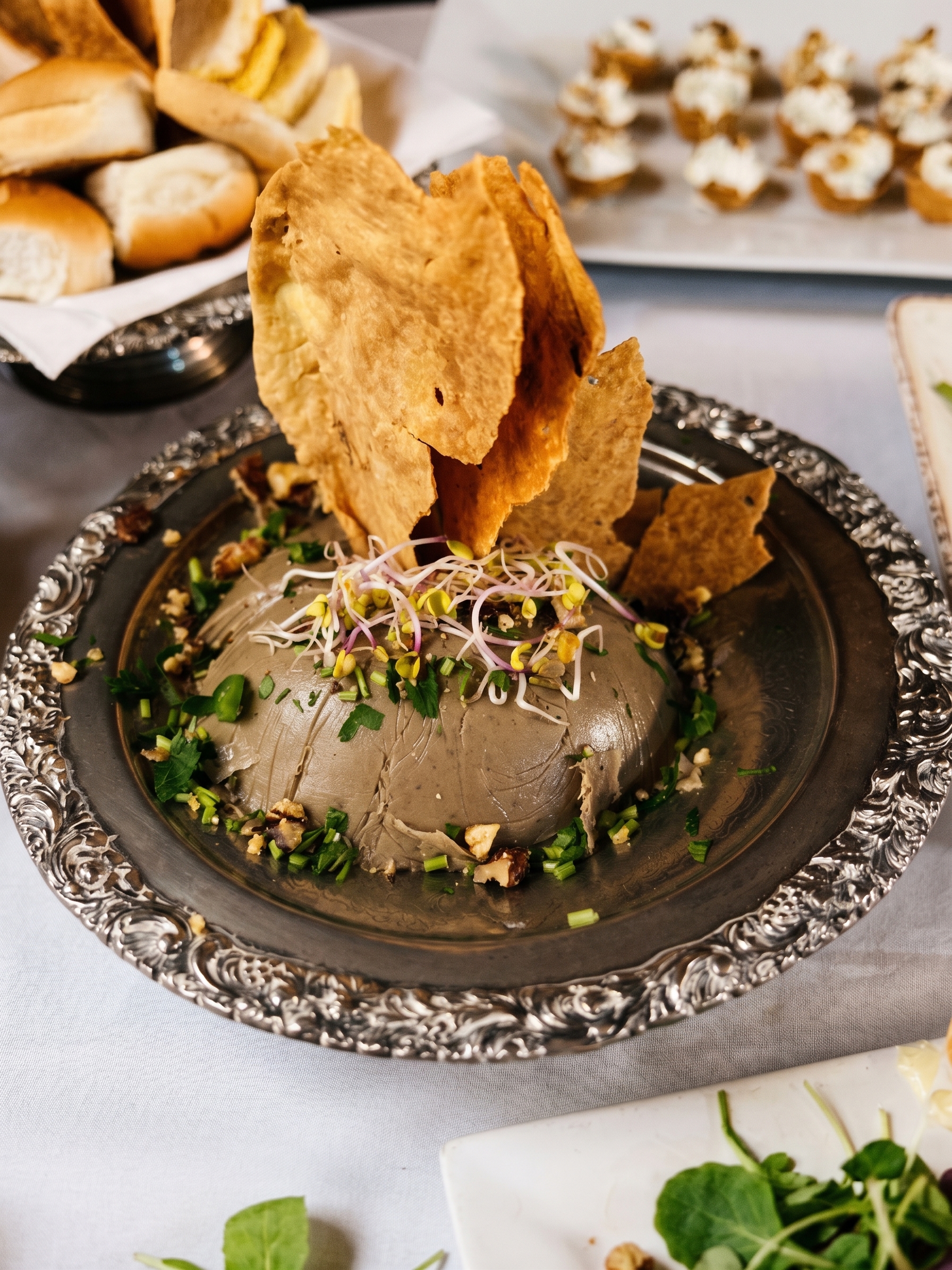 Pate casero en fuente de plata con crackers, brotes y panes