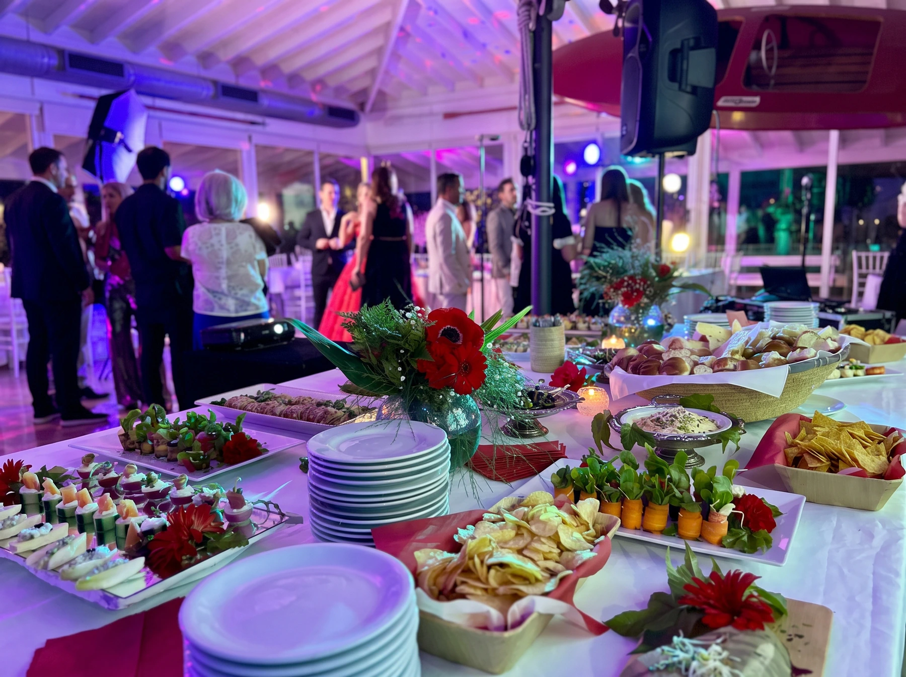Fiesta de noche con mesa de catering, platos, flores y luces violetas
