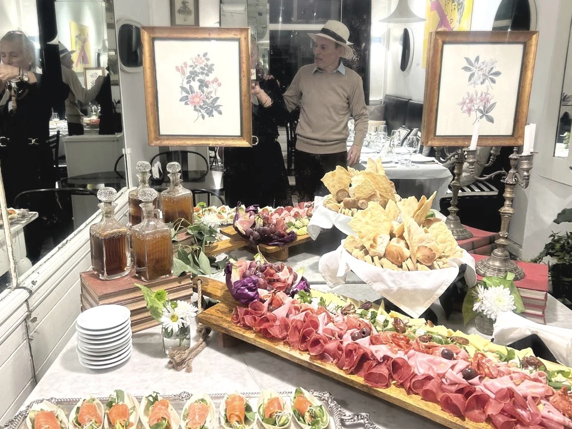 Mesa de evento con fiambres, panes, cuadros florales y candelabros